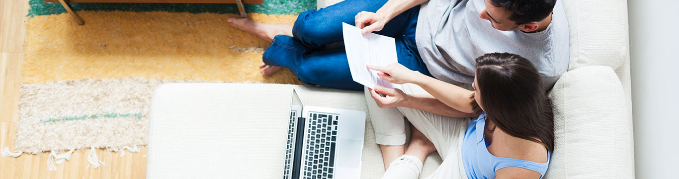 Couple reviewing paperwork together on a couch with a laptop nearby.